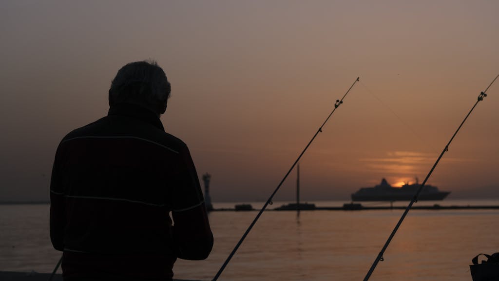 A man fishing at sunset with a cruise ship in the background