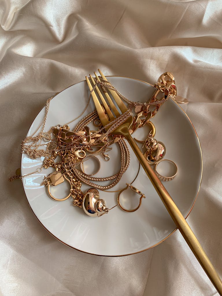 Golden Jewelry and Golden Fork on White Saucer on Beige Silk