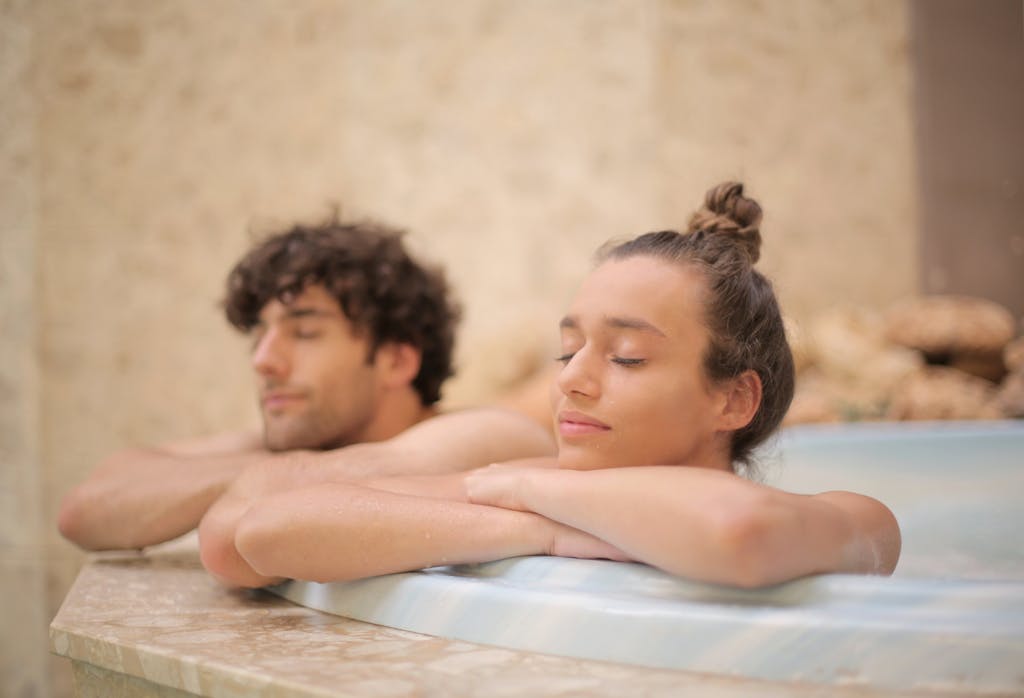 Happy cheerful man and woman with closed eyes bathing together leaning on bath edge during romantic weekend in luxury hotel in bathroom with marble interior