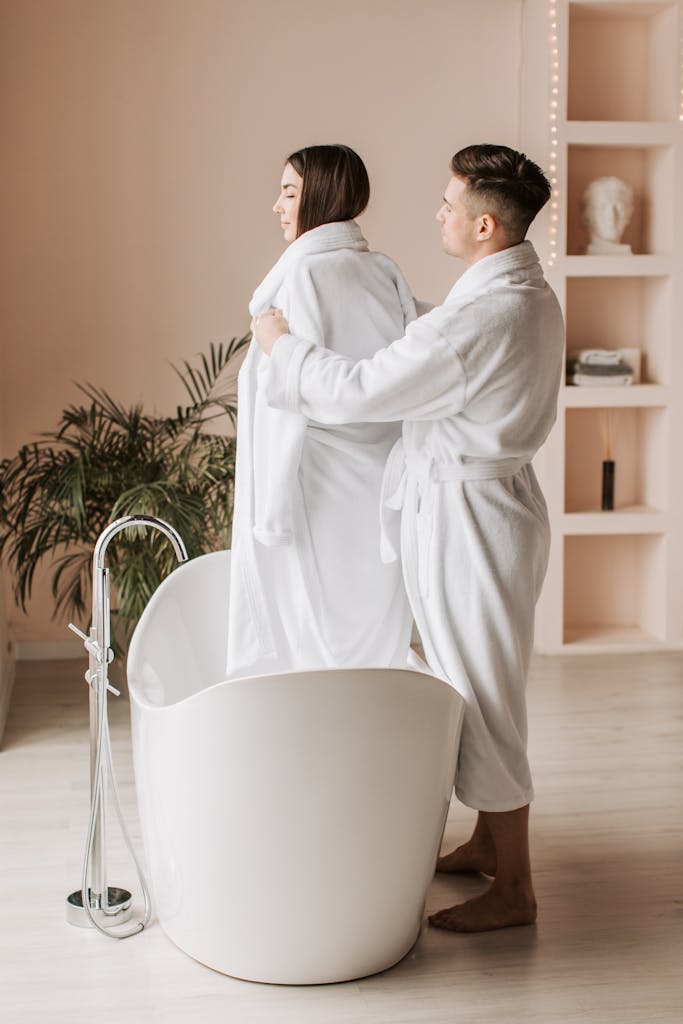 Man Helping His Partner to Take the Bathrobe Off While Standing in a Bathtub