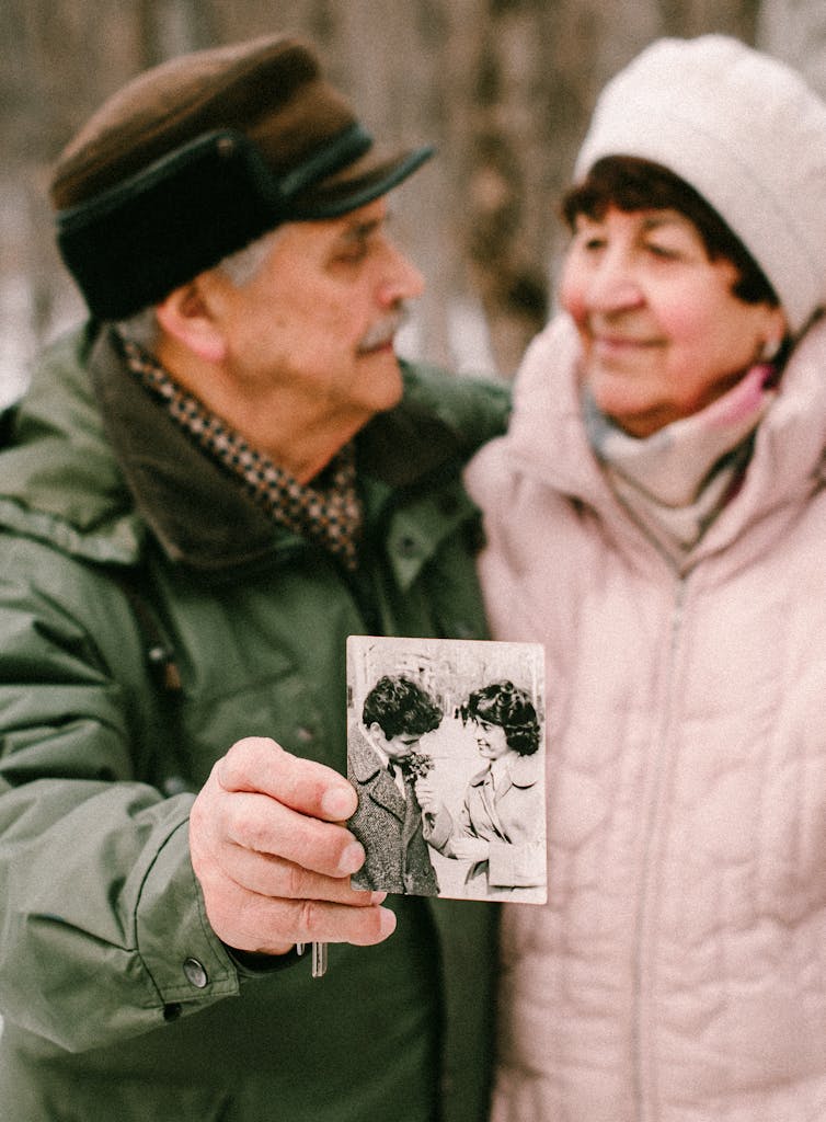 Man in Green Jacket Holding an Old Photo