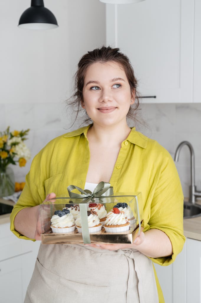Smiling female confectioner with packed cupcakes in kitchen