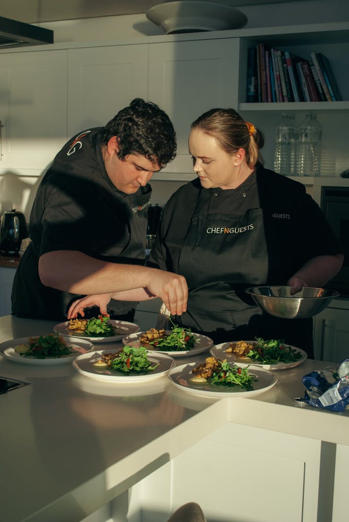 Two people in black aprons preparing food in a kitchen